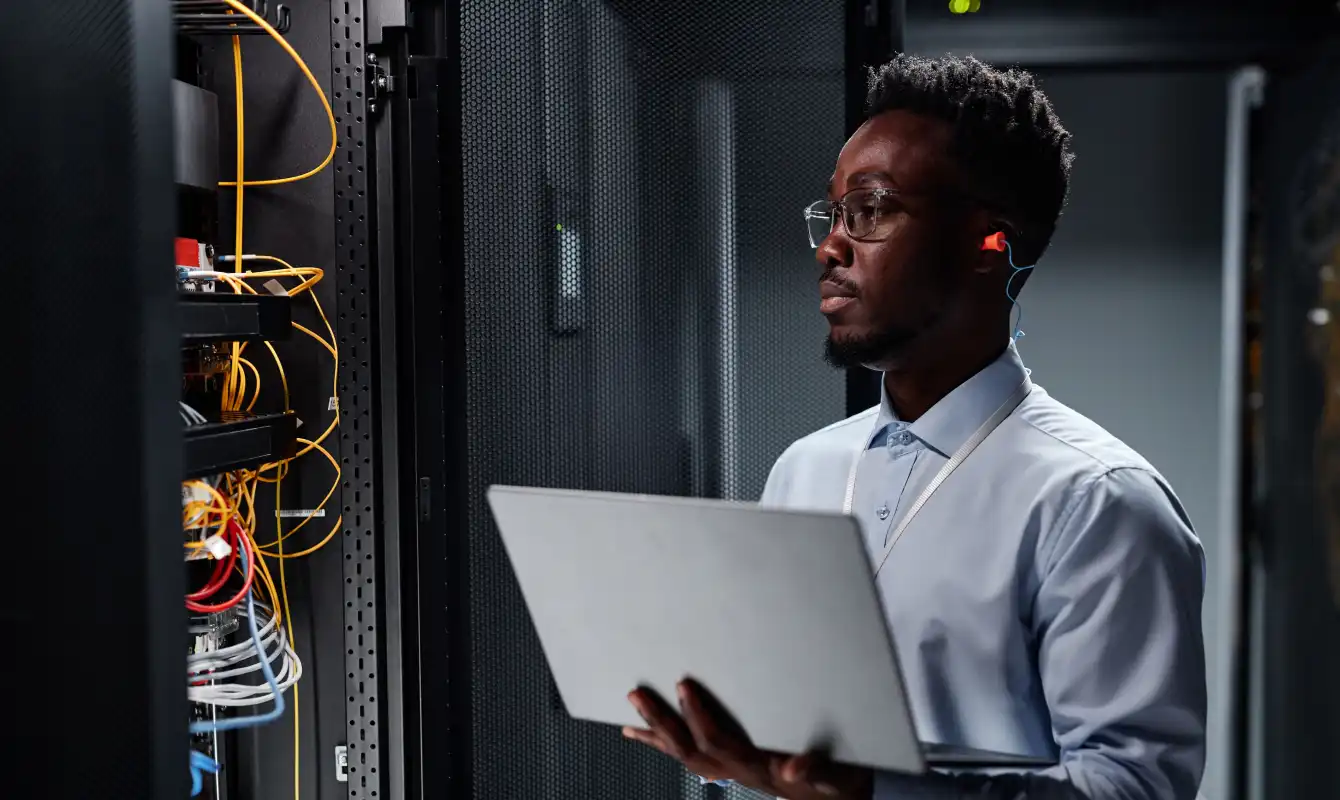 man with computer and earbud looking at server