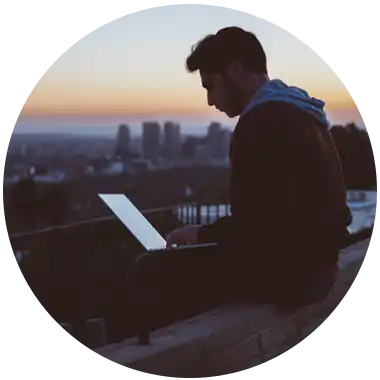 man on laptop in front of cityscape at dusk